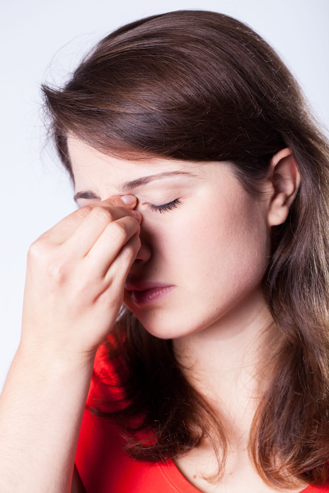 nosebleed-symptoms Woman pinching the bridge of her nose and looking distressed