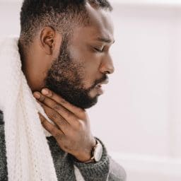 Side view of a man holding his throat with his mouth slightly open.