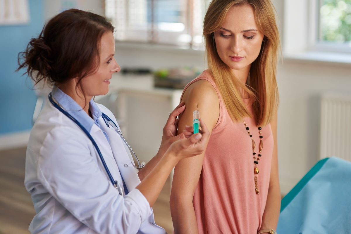 Allergy Immunotherapy Patient Woman in a doctors office getting a shot to the arm from her doctor. She is looking down at her arm as her doctor looks at the her with her thumb over the plunger.