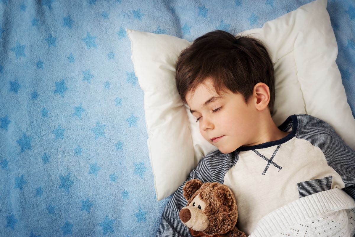 Pediatric-snoring-symptoms Child sleeping in bed with a teddy bear tucked under their arm