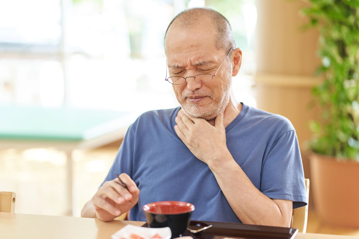 Swallowing-Disorders-symptoms Older man at home closing eyes in pain with his hand placed on his upper chest and bottom of throat