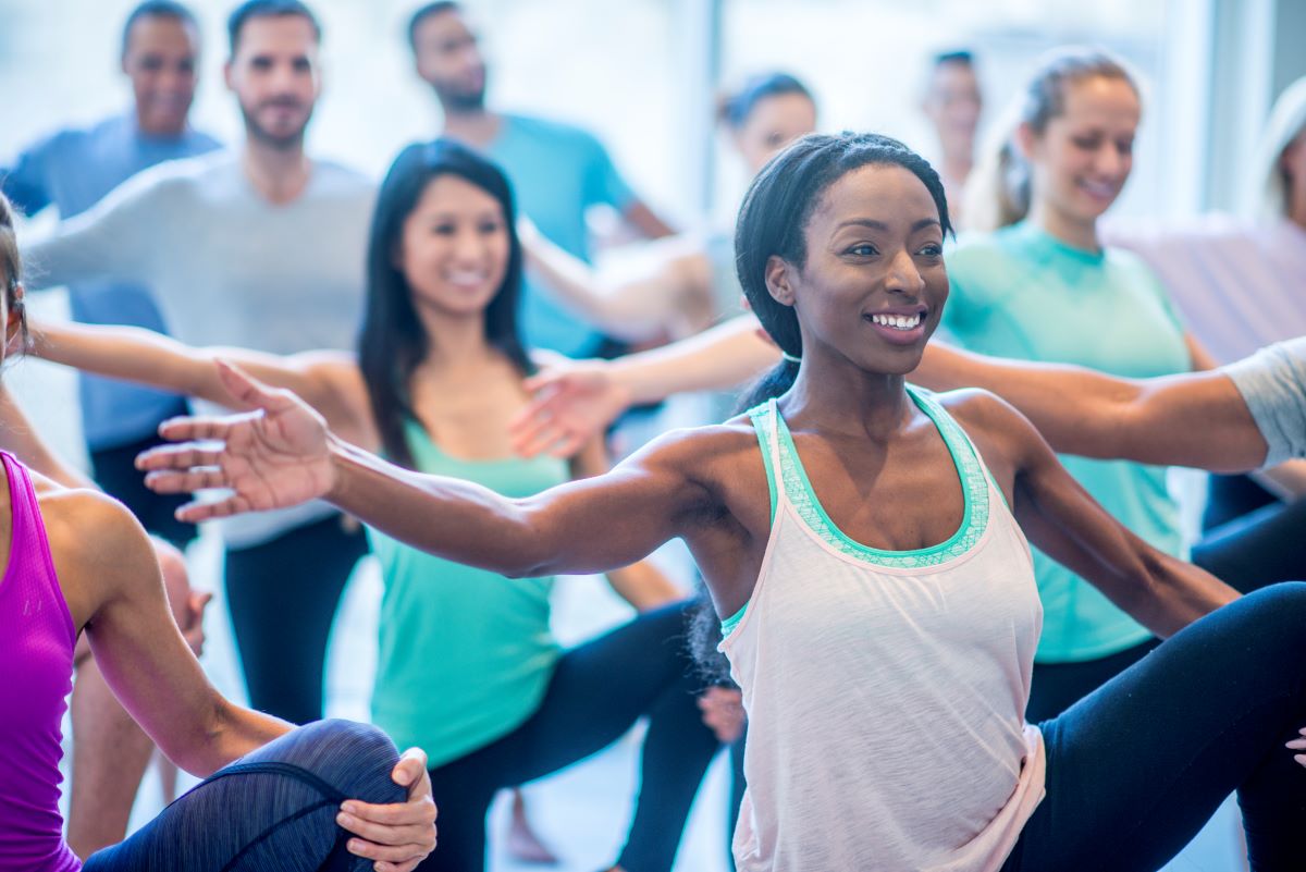 results of balance treatments Focus on a woman in a floor class who is doing stretches with women and men. Everyone is balancing on one leg. The other leg is held up with one hand by the knee. The opposite arm on the standing leg is held outward and horizontally.