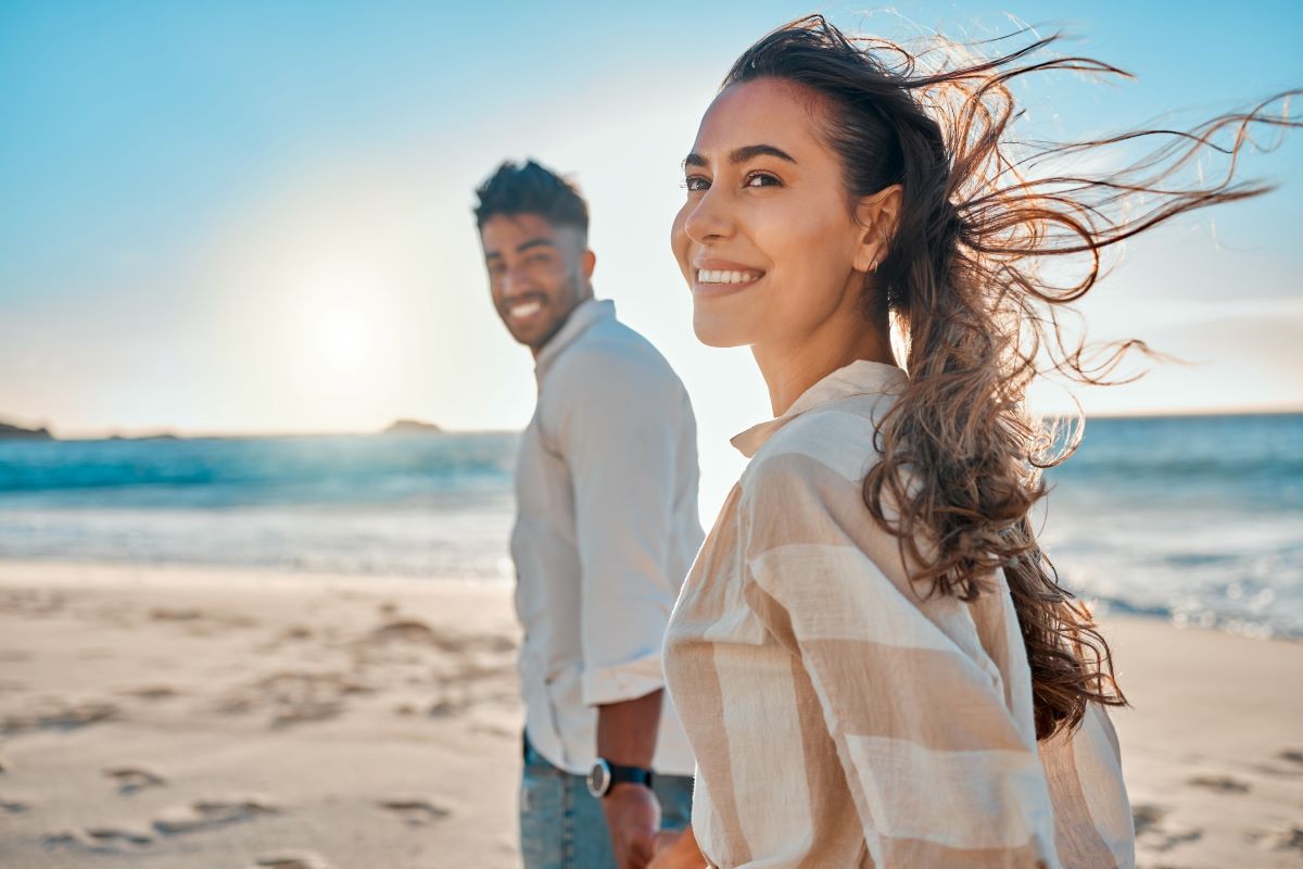 Sleep-surgery-results A heterosexual couple holding hands and walking on the beach as the wind blows the womans hair behind her. It is after midday and the ocean can be seen behind the couple.