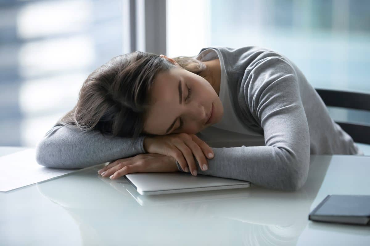 sleep narcolepsy treatment Young woman who has fallen asleep on an office desk with a closed laptop underneath her. She is resting her head on her crossed arms.