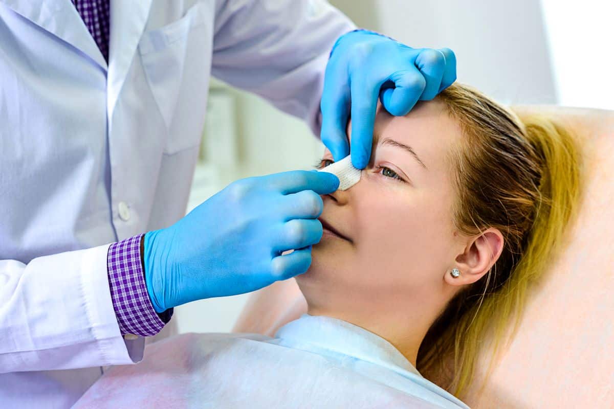 nasal fracture patient care doctor wearing blue rubber gloves is placing a bandage over the bridge of a female patients nose