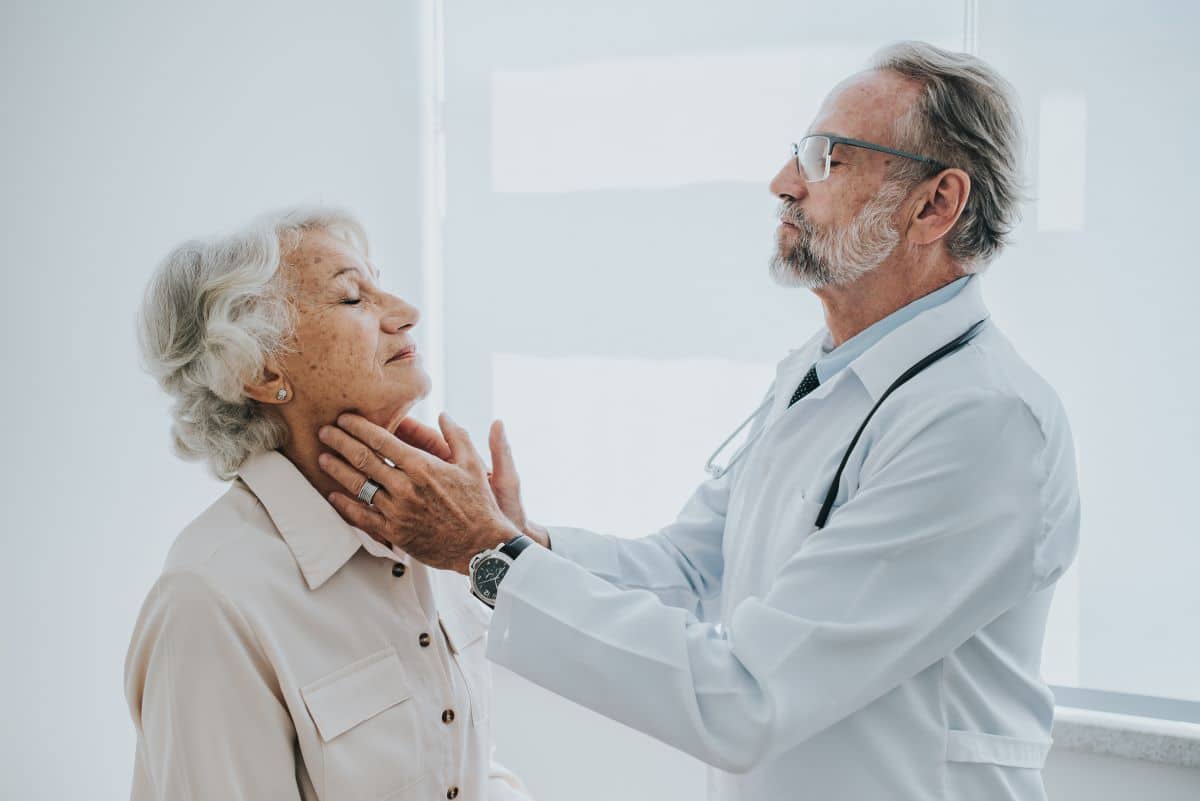 tonsillitis-symptoms doctor in a medical setting is feeling an older patients throat for indications of tonsillitis
